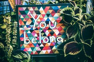 A colourful sign that says "you belong" surrounded by plants